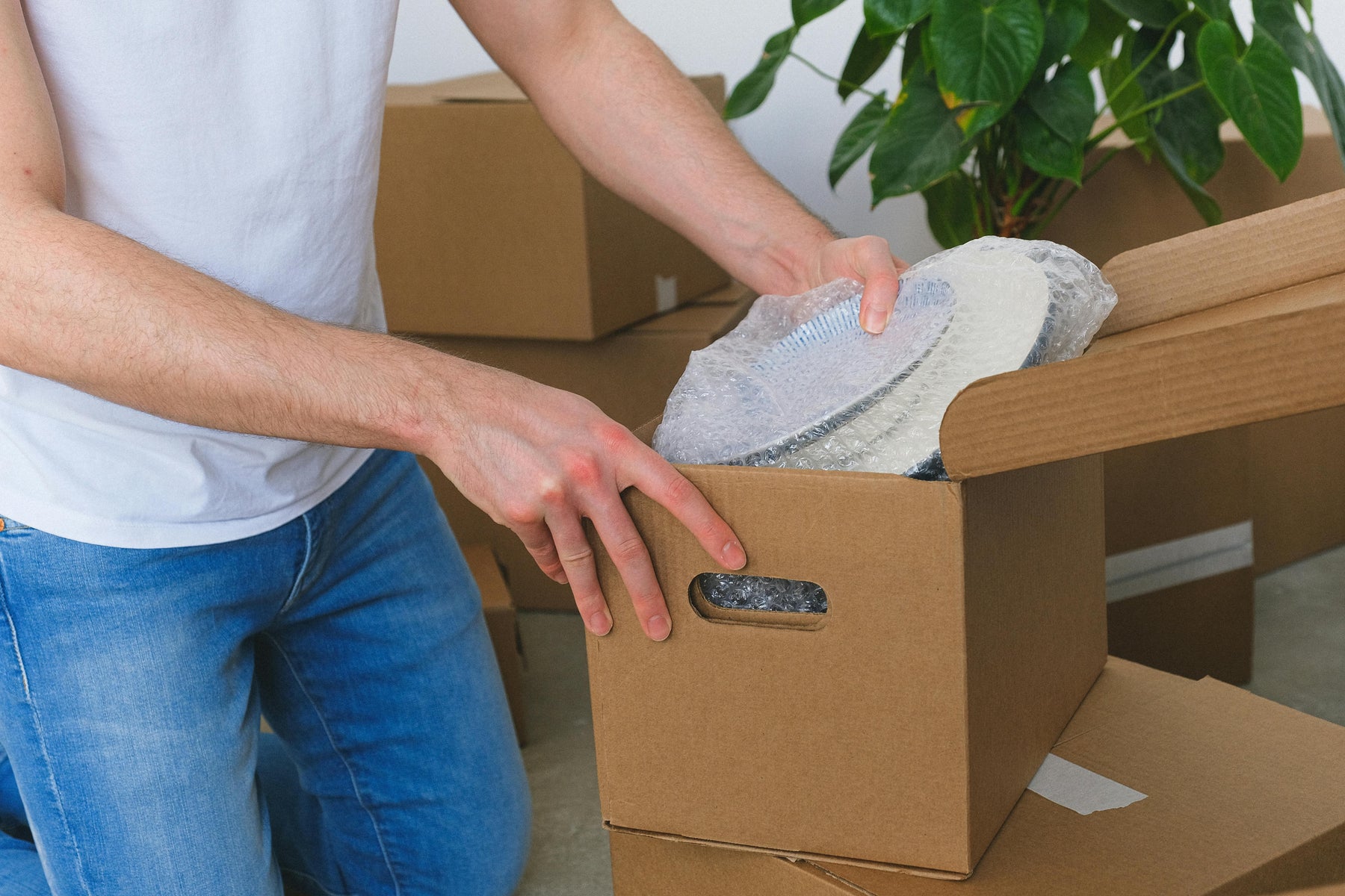 Person packing a cardboard box with bubble wrap, illustrating traditional protective packaging compared to modern air cushion alternatives in e-commerce.
