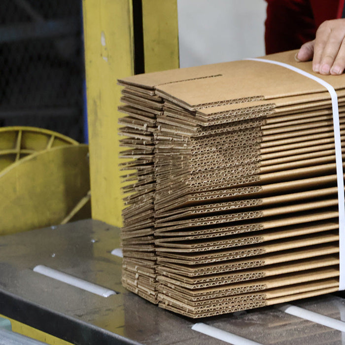 Stack of flat cardboard boxes tied with a white strap on a production line, ready for packaging or delivery.