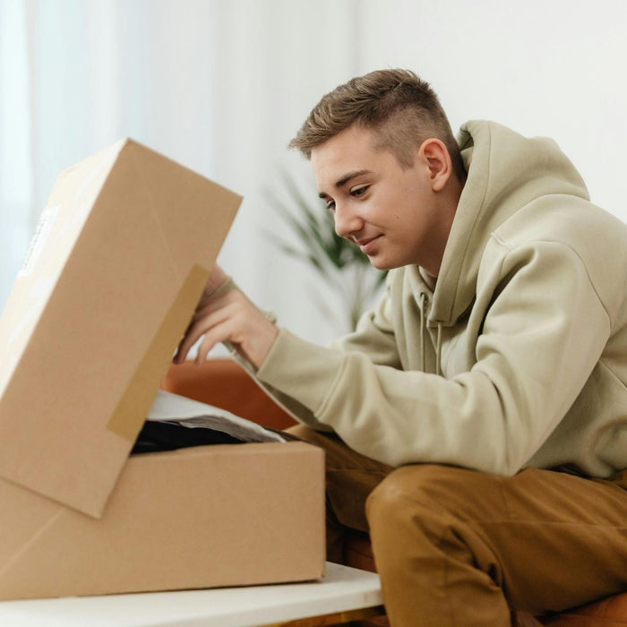 Young man unboxing a parcel at home — illustrating customer experience with e-commerce packaging.