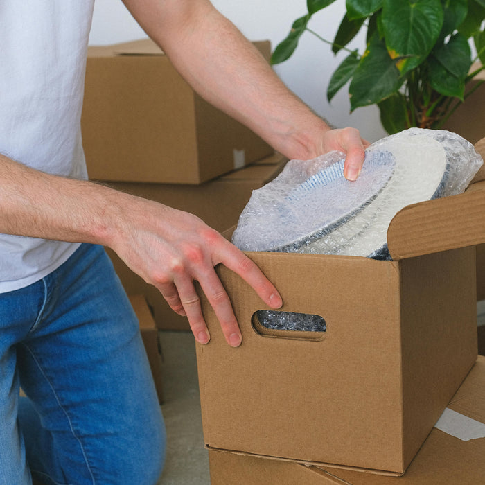 Person packing a cardboard box with bubble wrap, illustrating traditional protective packaging compared to modern air cushion alternatives in e-commerce.